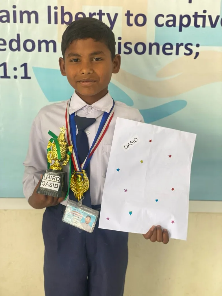Qasid holding a trophy, medals, and a certificate